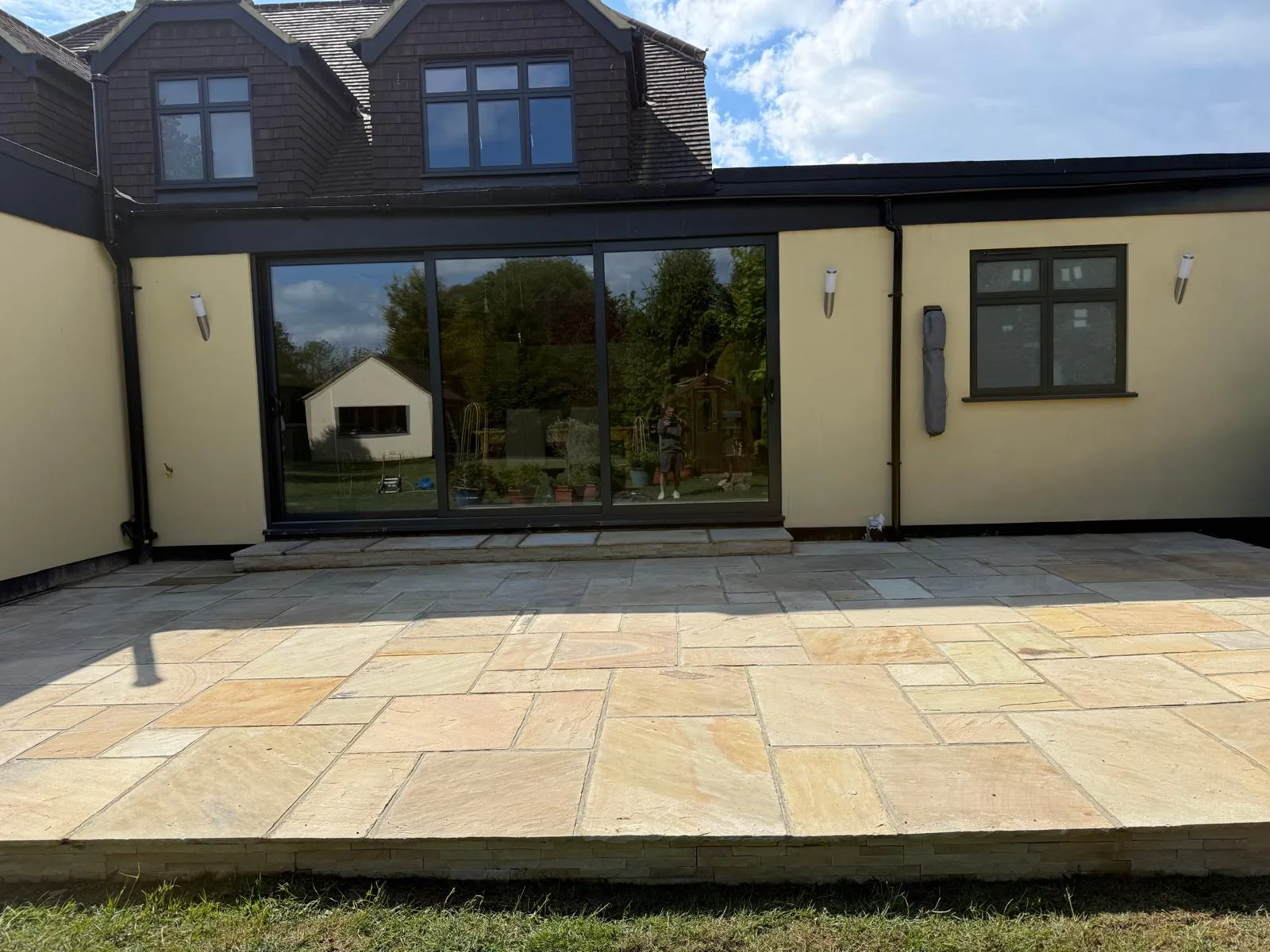 Indian sandstone patio wrapping around a rendered house with anthracite bifold doors, laid by Prestige Landscapes in Downe Village