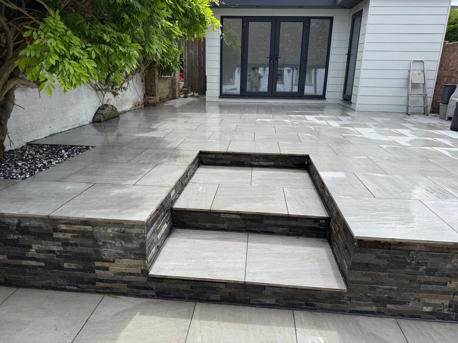 Grey porcelain patio with split-face stone steps leading up to black bifold doors, laid by Prestige Landscapes in Farnborough Village